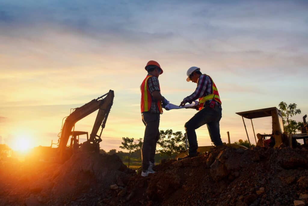 two men on a construction site at sunset reviewing surveys